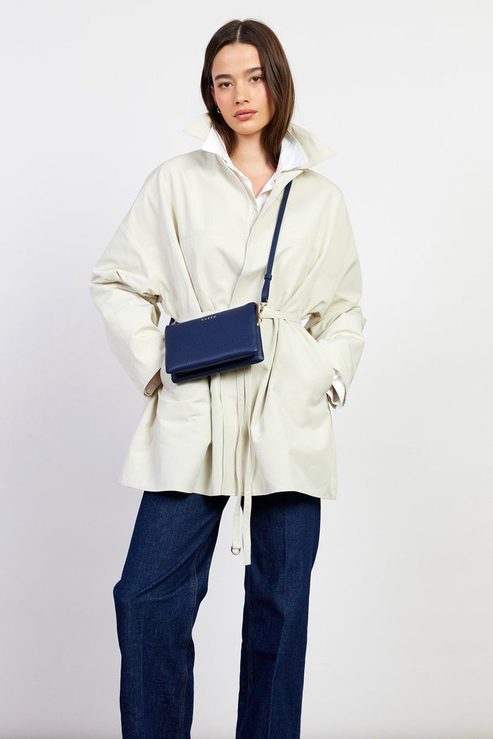 Person wearing a cream jacket and dark pants with a blue bag on a white background