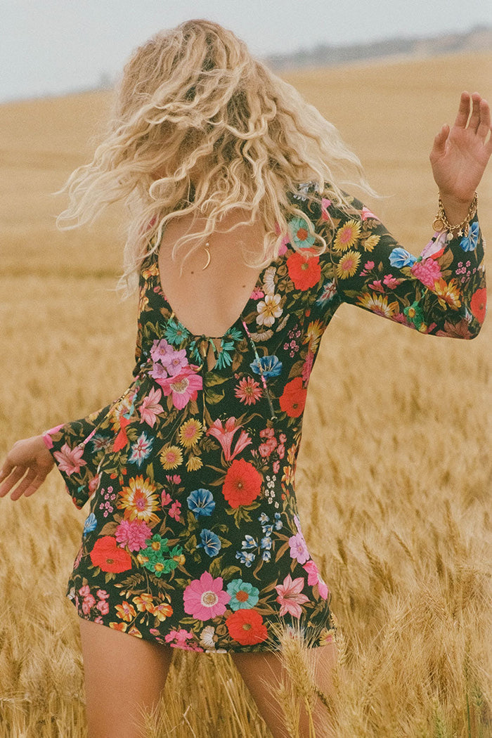 Model's back view in floral viscose mini dress, open back with tie detail and wide-cuff long sleeves, wheat field setting