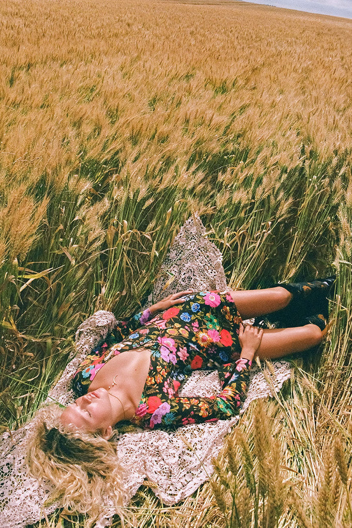 Model lying in a wheat field wearing the floral bias mini dress, midriff visible with front ties open