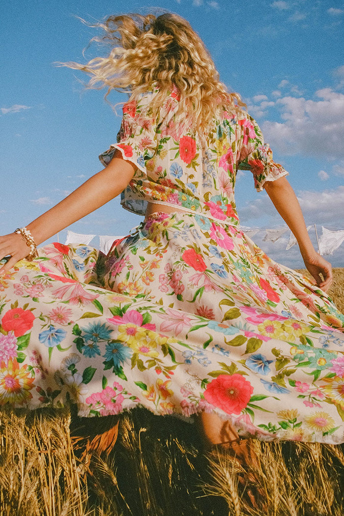 Back view of model in floral TENCEL skirt with hi-lo frayed hem, twirling through a golden wheat field