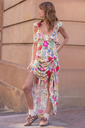 Woman wearing a colorful floral dress standing against a beige wall.