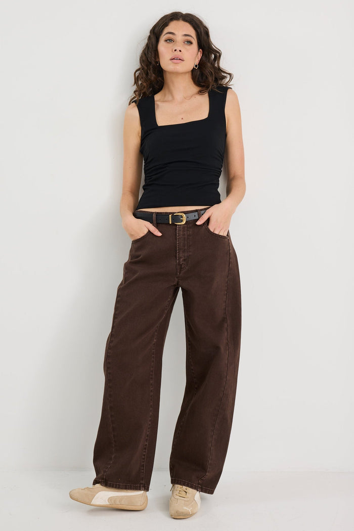 Woman wearing a black tank top and brown pants on a white background