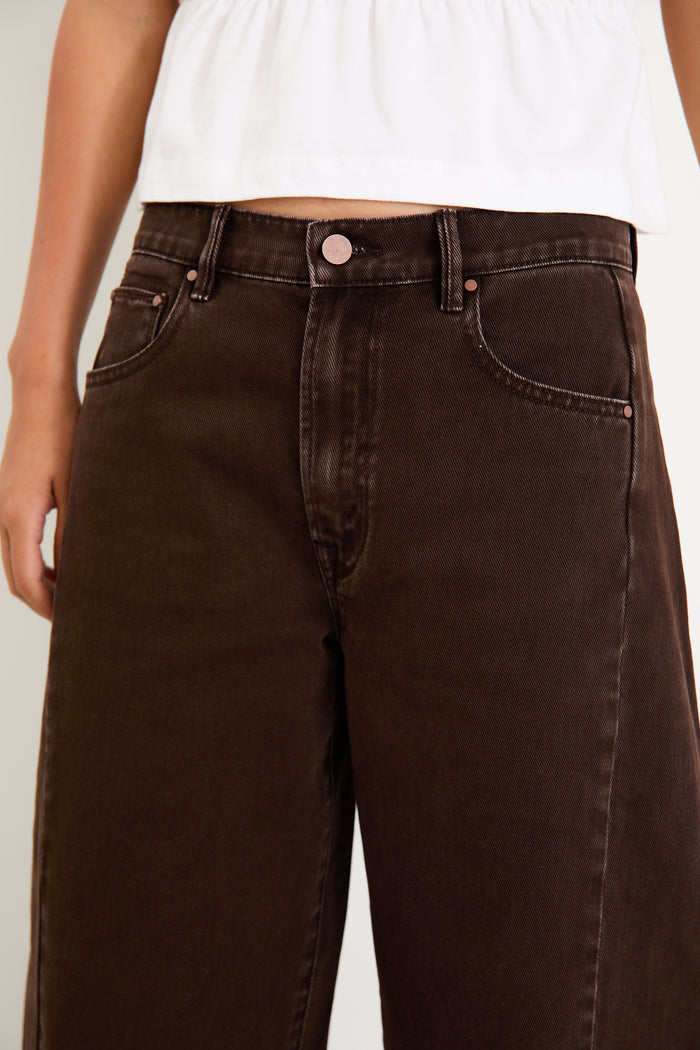 Woman wearing a white top and brown pants on a white background.