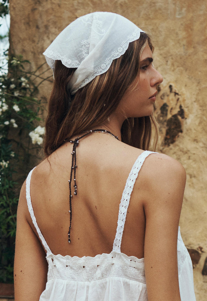Back view of model wearing white organic cotton headscarf with scallop edge and embroidered floral artwork