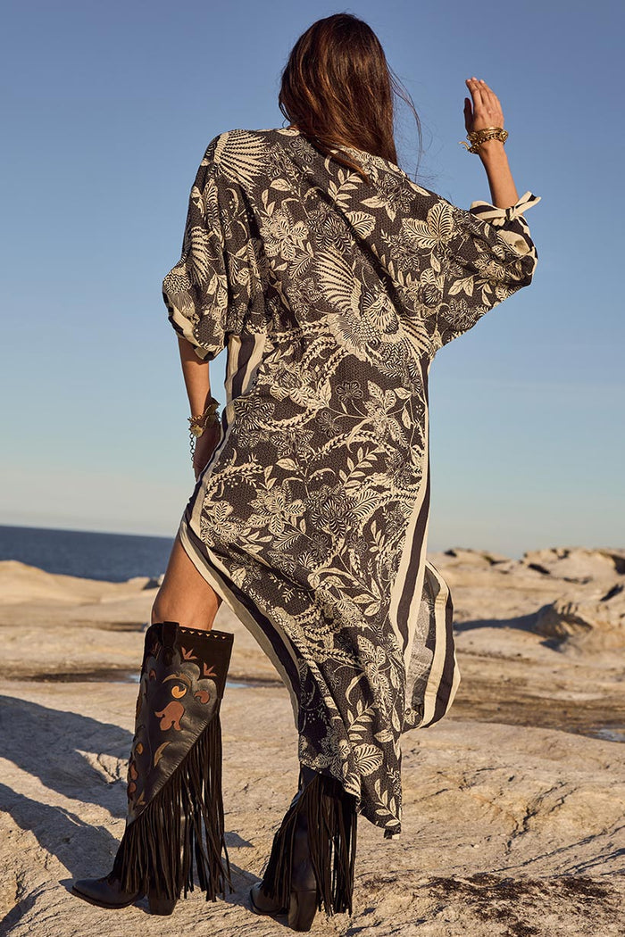 Back view of Volcano Goddess Kaftan in Liquorice, showing side stripe detail and dropped shoulder on rocky background