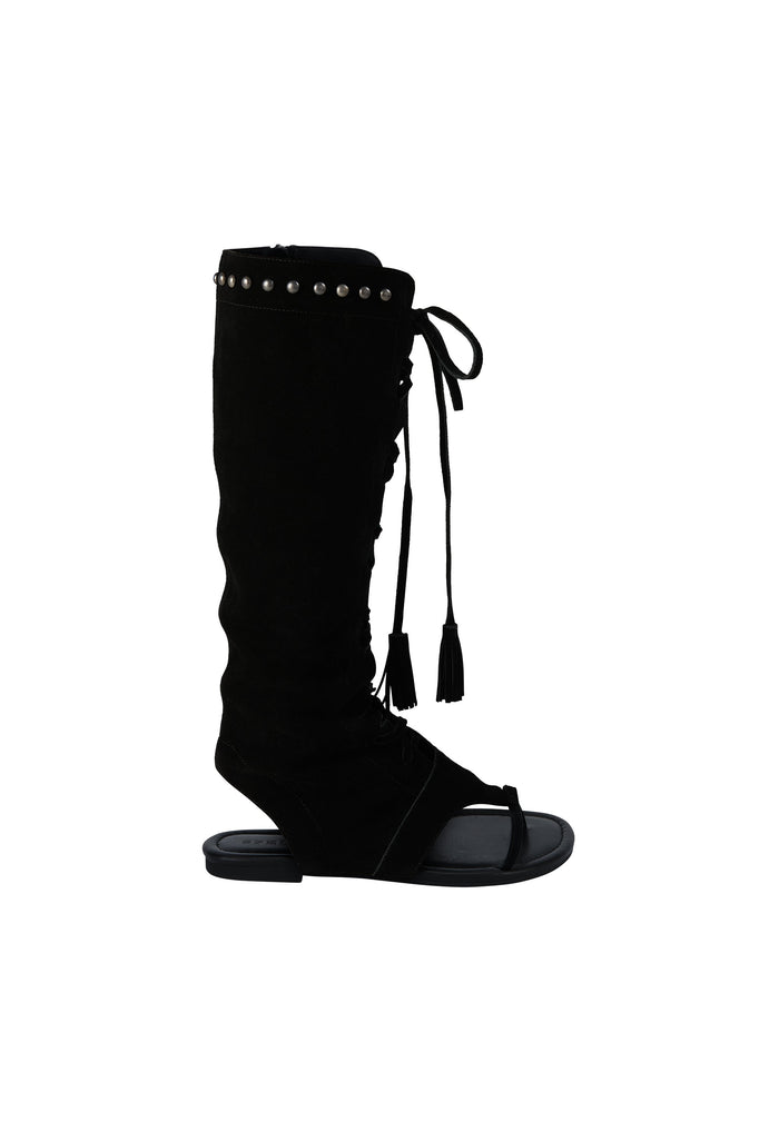 A black knee-high wedge sandal boot with silver studs along the top collar, lace-up front details, and tassel ties, shown against a plain white background.