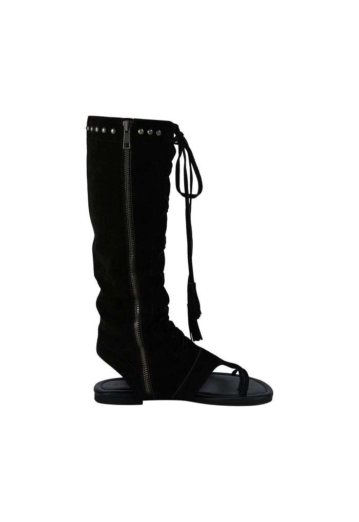 A black suede knee-high boot with a side zipper, silver studs, and a lace-up front detail, shown against a plain white background.