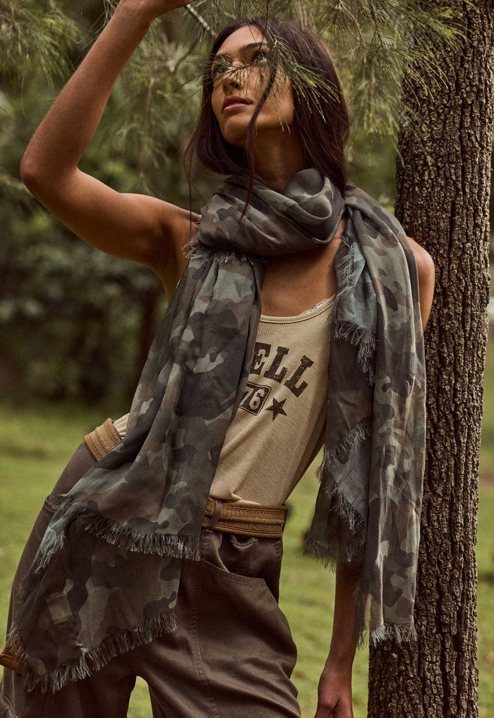 Front view of camo green modal travel scarf with frayed edges, draped loosely around model's neck outdoors