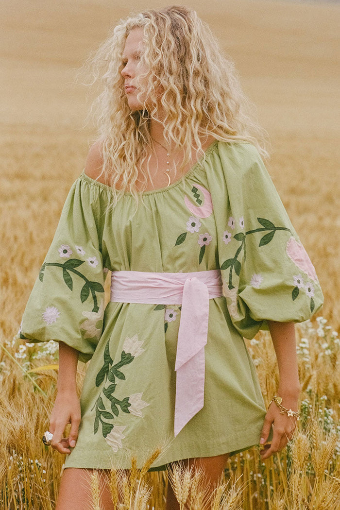 Front view of Wonderland Dress in Lime Essence with floral appliqué, puff sleeves, elastic neck, and pink sash belt