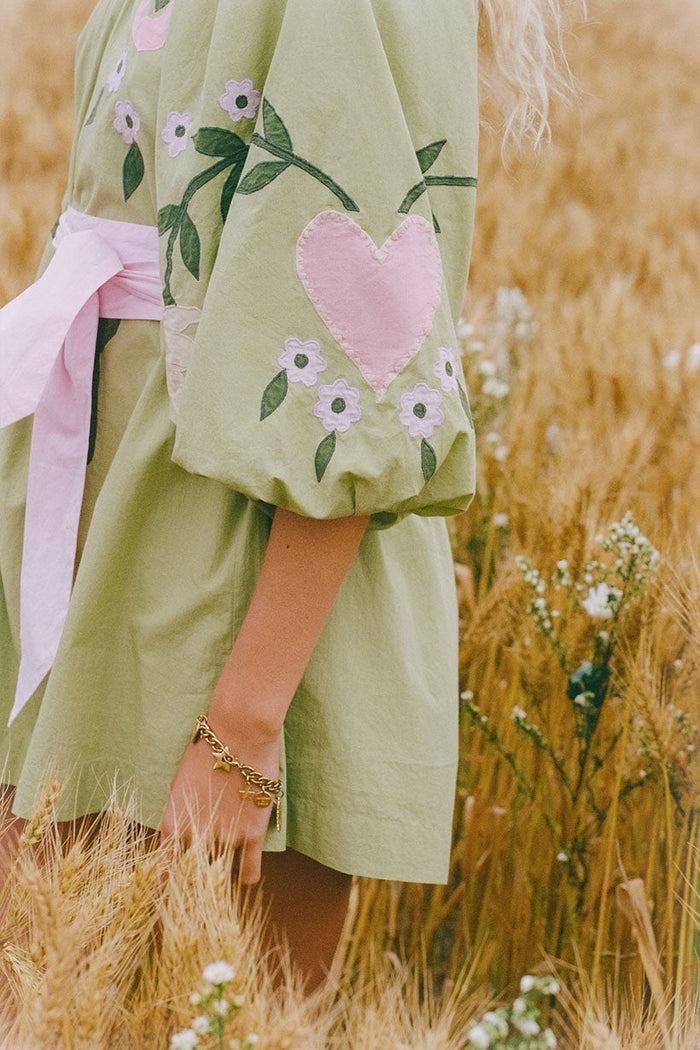 Side detail of lime green organic cotton puff sleeve with pink heart applique and floral embroidery, pink sash tie visible