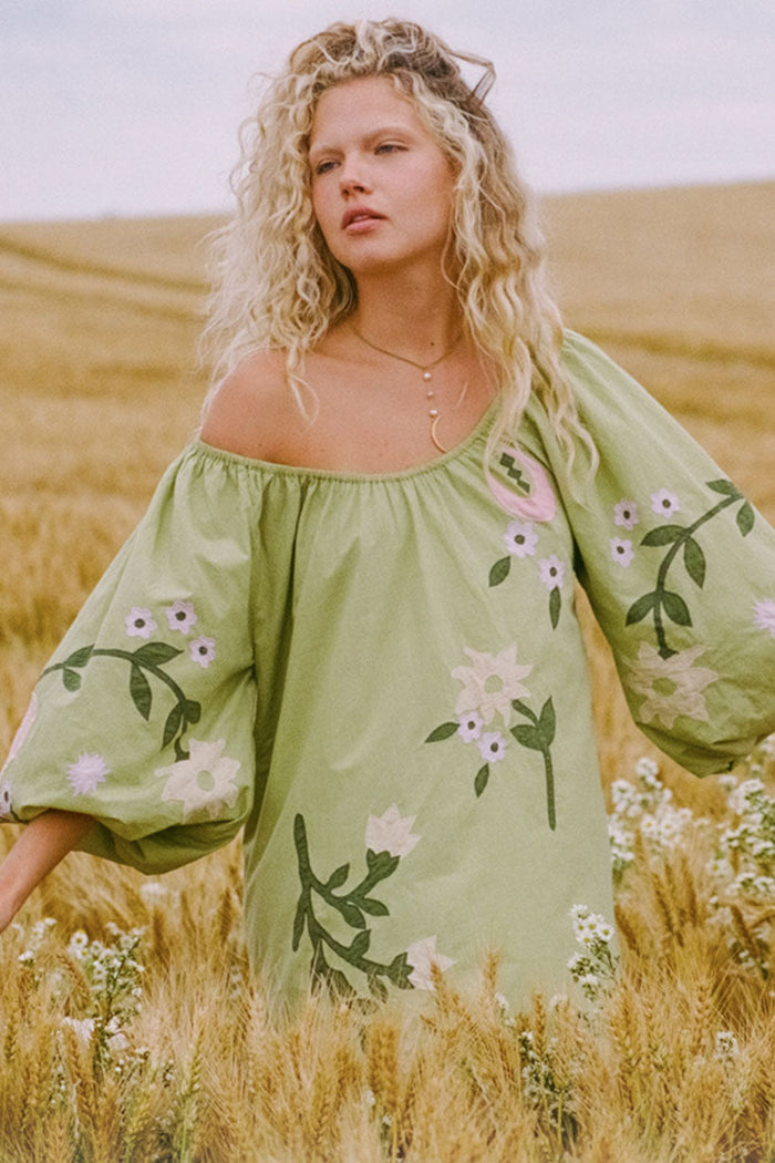 Front-facing model shot of lime green organic cotton mini dress with floral appliqué, puff sleeves, elastic neck