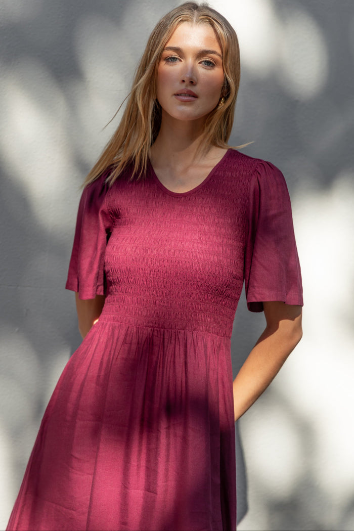 Woman wearing a burgundy dress standing against a blurred natural background