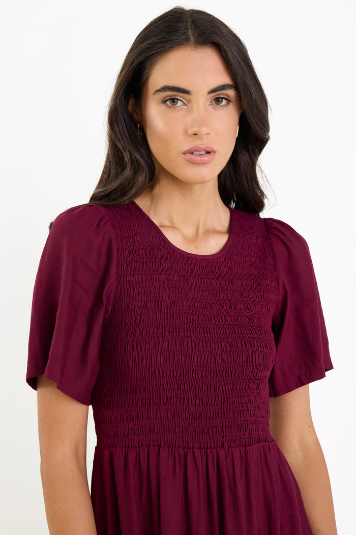 Woman wearing a burgundy dress with puff sleeves on a white background