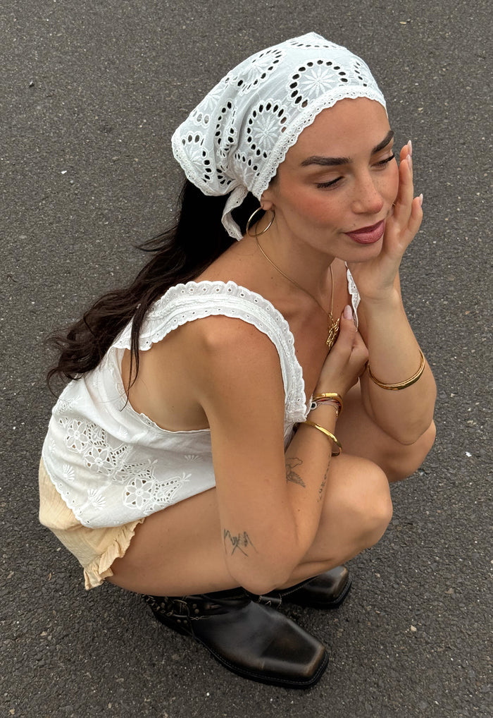 Model crouching, wearing Yaya Headscarf tied at nape, broderie anglaise detail and scallop trim visible