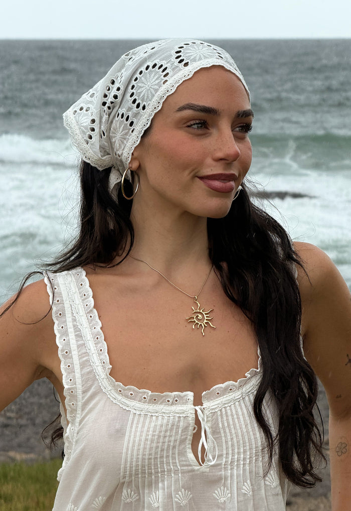 Close-up of broderie anglaise headscarf tied as headwrap, scallop trim detail, styled at ocean with white top