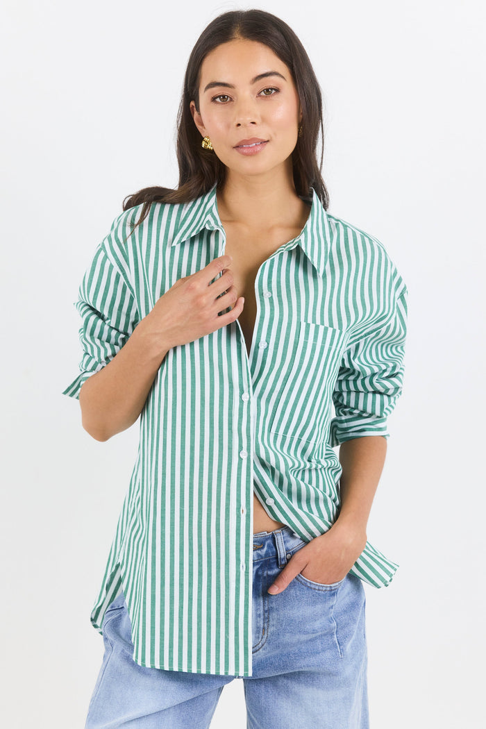 Woman wearing a green and white striped shirt with rolled-up sleeves and light blue jeans on a white background