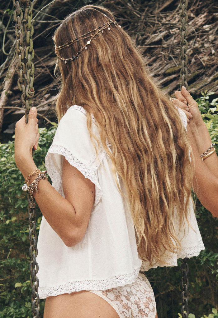 Back view of a model wearing antique white organic cotton crop blouse with custom lace trim hem on swing