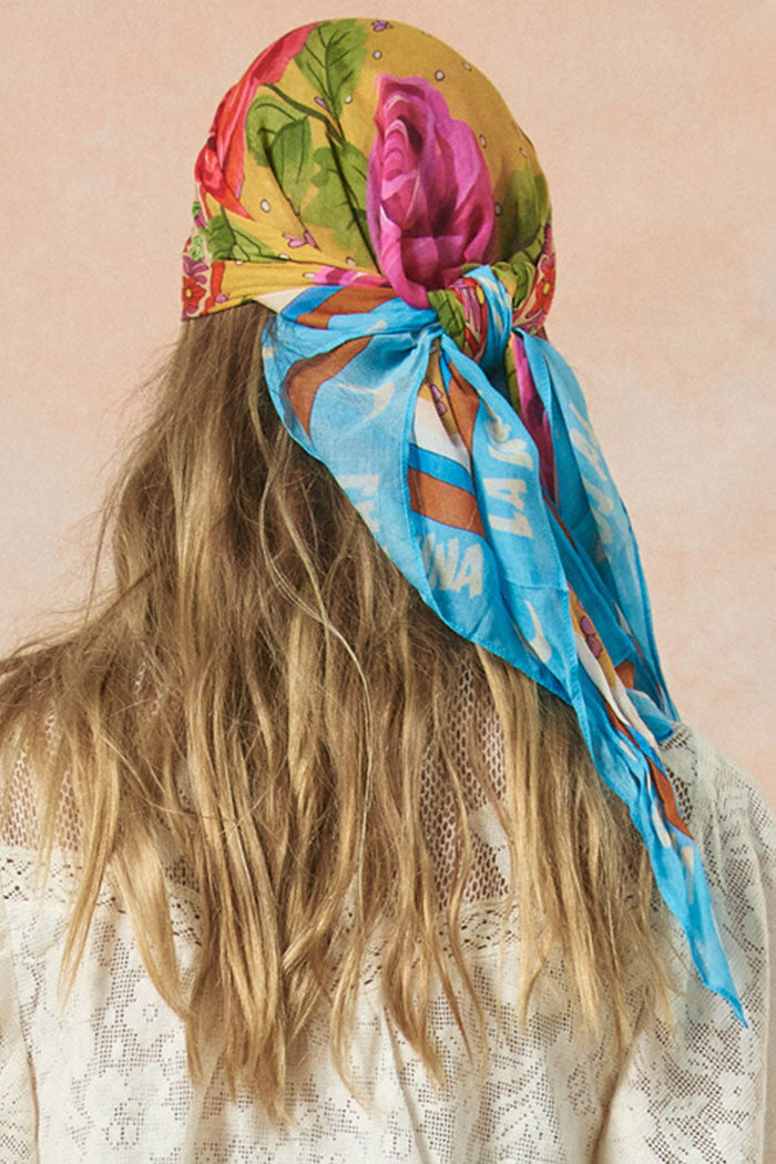 Back view of floral Aphrodite scarf tied as a headscarf, trailing over loose waves, with lace top beneath