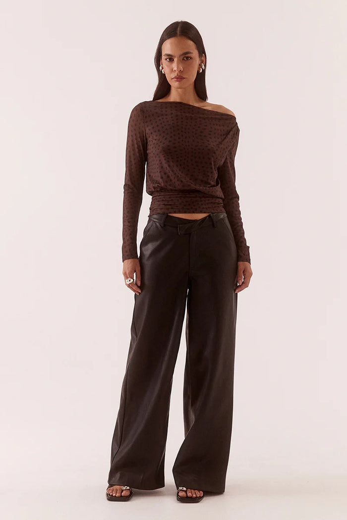 Woman wearing a brown off-shoulder top and dark pants on a white background