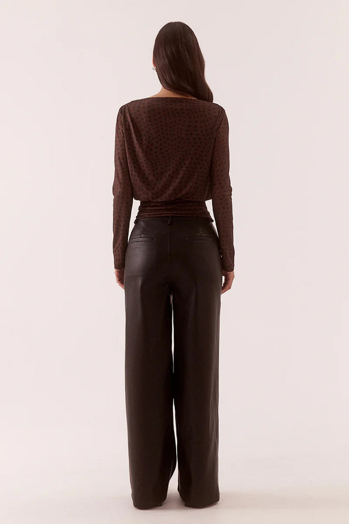 Person wearing a brown top and black leather pants on a white background